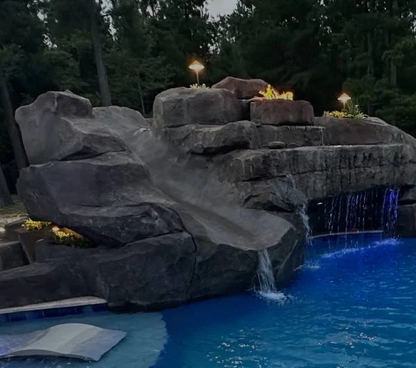 Evening pool feature with illuminated waterfalls and fire above the sculpted rock